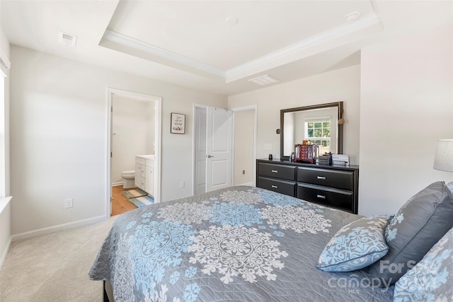 bedroom with ensuite bathroom, light carpet, and a raised ceiling