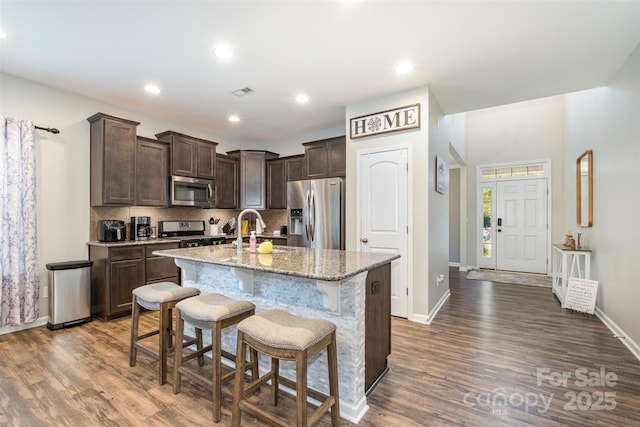 kitchen featuring light stone countertops, dark hardwood / wood-style floors, stainless steel appliances, a kitchen island with sink, and sink