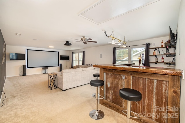 carpeted cinema room with indoor bar, ceiling fan, and a healthy amount of sunlight