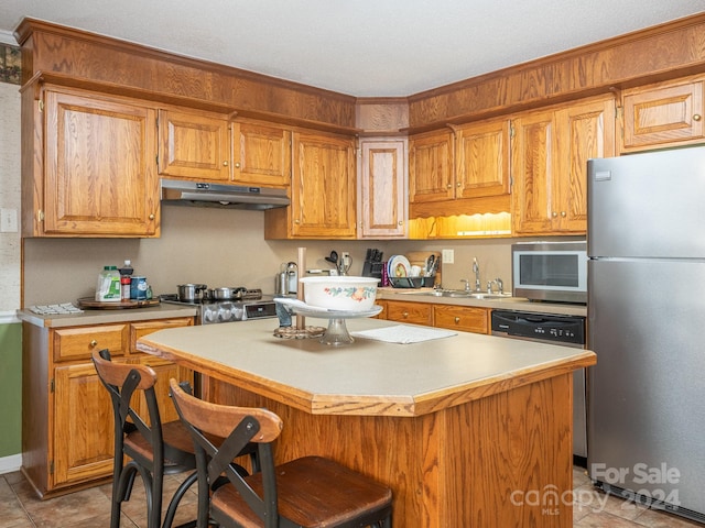 kitchen featuring a breakfast bar, dishwasher, sink, stovetop, and stainless steel refrigerator