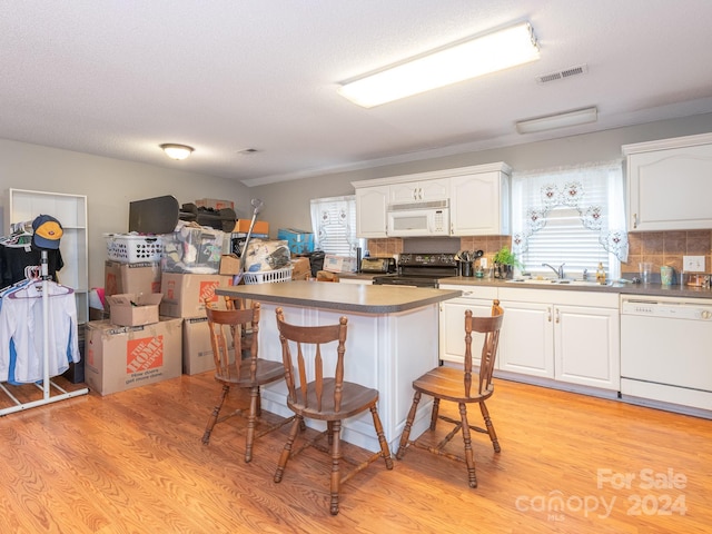 kitchen featuring white appliances, a kitchen breakfast bar, light wood-type flooring, tasteful backsplash, and white cabinetry