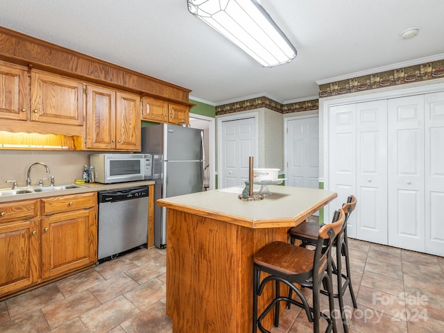 kitchen featuring a kitchen bar, stainless steel appliances, crown molding, sink, and a center island