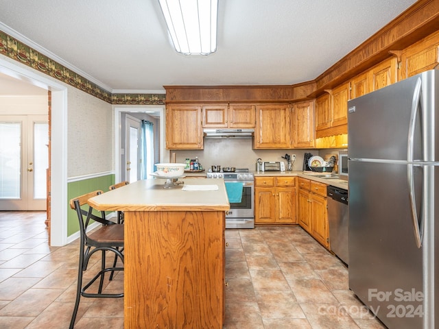 kitchen with a kitchen breakfast bar, ornamental molding, a textured ceiling, stainless steel appliances, and a center island