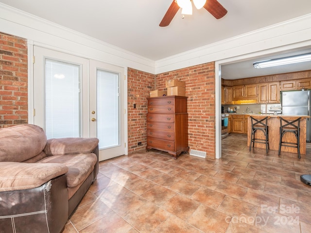 living room featuring french doors, ceiling fan, ornamental molding, and brick wall