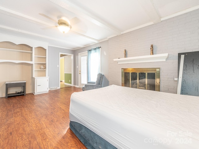 bedroom with hardwood / wood-style floors, a brick fireplace, ceiling fan, beamed ceiling, and brick wall