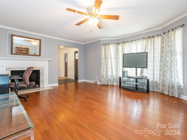 unfurnished living room with a fireplace, wood-type flooring, ceiling fan, and ornamental molding