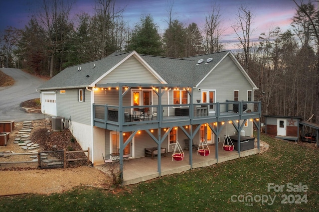 back house at dusk featuring a patio area, a jacuzzi, a wooden deck, and central AC