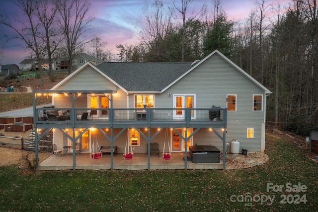 back house at dusk with a deck, a patio, a yard, and a hot tub