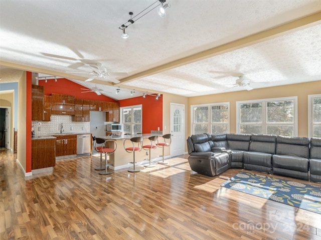 living room featuring wood-type flooring, vaulted ceiling with beams, a textured ceiling, sink, and ceiling fan