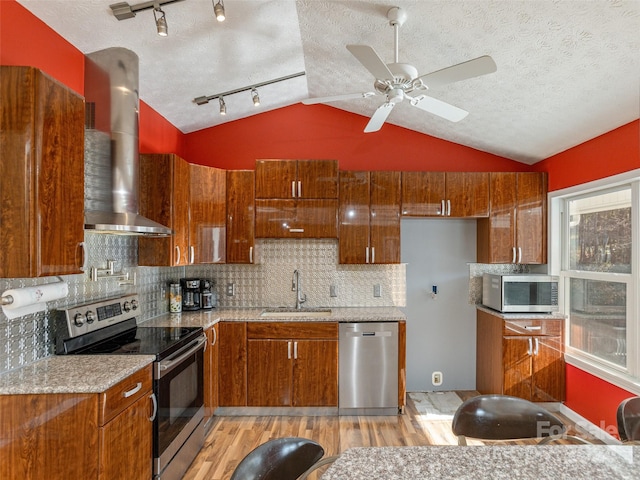 kitchen featuring light stone counters, stainless steel appliances, light wood-type flooring, sink, and wall chimney exhaust hood