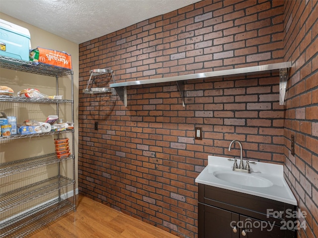 bathroom with hardwood / wood-style floors, brick wall, a textured ceiling, and vanity