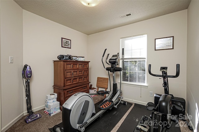 exercise room with dark carpet and a textured ceiling