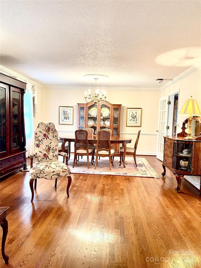 dining area with crown molding, wood-type flooring, a textured ceiling, and a chandelier