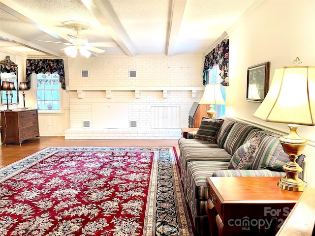 living room with ceiling fan, a brick fireplace, beamed ceiling, brick wall, and ornamental molding