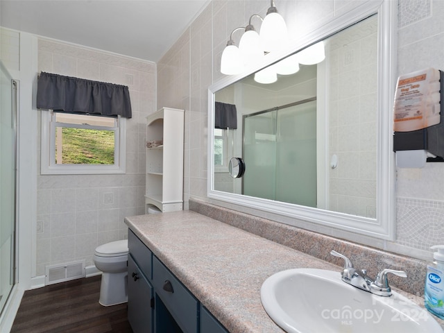 bathroom with tile walls, hardwood / wood-style floors, vanity, and a shower with door