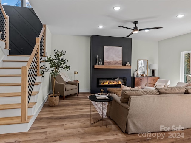 living room with a large fireplace, light hardwood / wood-style flooring, and ceiling fan