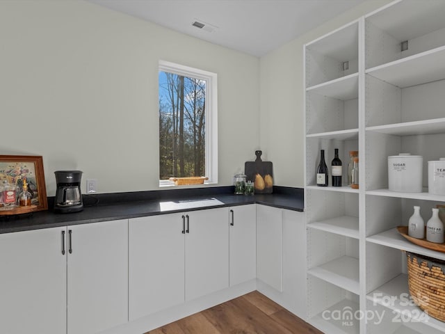 bar with light wood-type flooring and white cabinetry