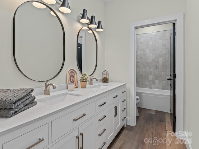 full bathroom featuring hardwood / wood-style floors, vanity, toilet, and tiled shower / bath combo