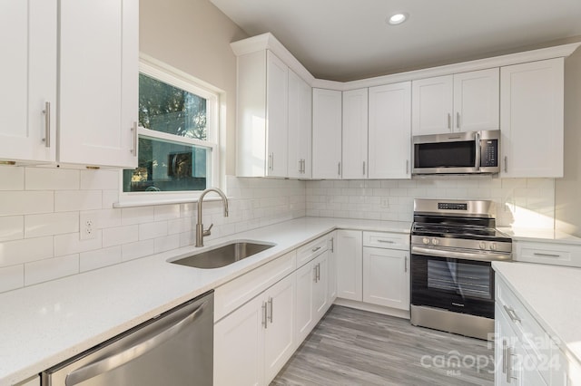 kitchen with sink, tasteful backsplash, light hardwood / wood-style floors, white cabinets, and appliances with stainless steel finishes