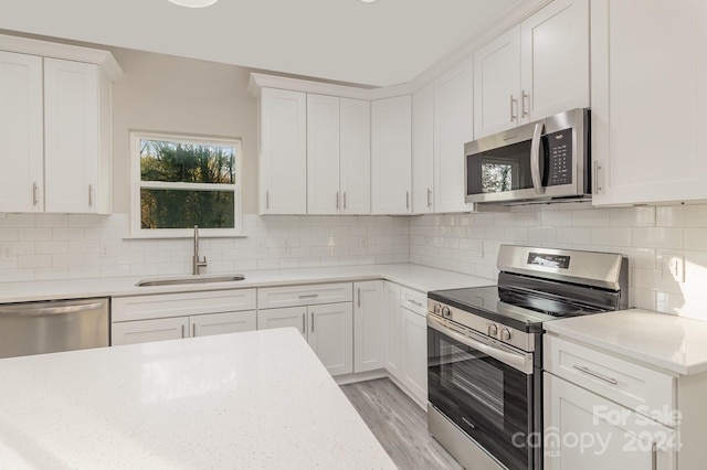 kitchen featuring white cabinetry, sink, light hardwood / wood-style floors, backsplash, and stainless steel appliances