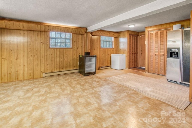 basement with stainless steel fridge, white refrigerator, baseboard heating, and wooden walls