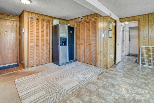 kitchen featuring stainless steel refrigerator with ice dispenser, a textured ceiling, and wood walls