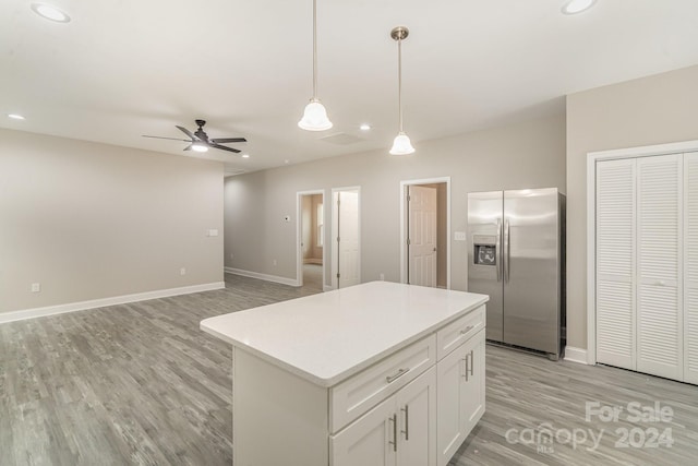 kitchen featuring stainless steel fridge, a kitchen island, ceiling fan, decorative light fixtures, and white cabinetry