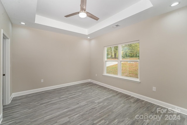 unfurnished room featuring a raised ceiling, ceiling fan, and dark hardwood / wood-style flooring