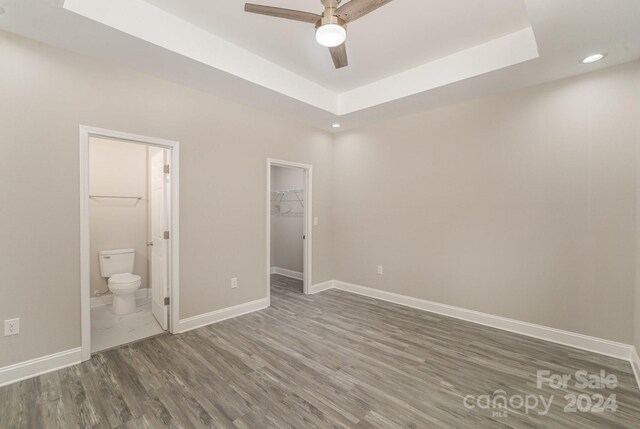 unfurnished bedroom featuring a tray ceiling, ceiling fan, dark wood-type flooring, a spacious closet, and a closet