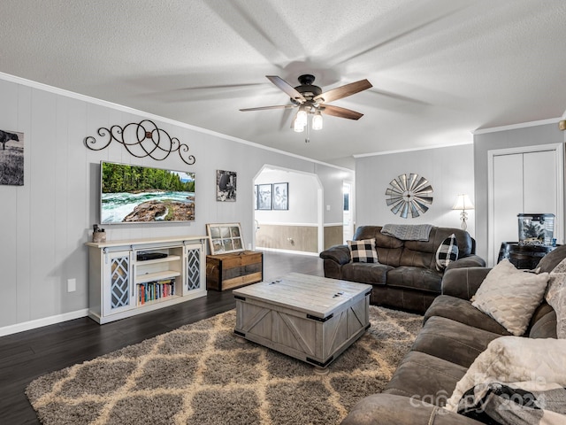 living room with a textured ceiling, ceiling fan, wooden walls, crown molding, and dark hardwood / wood-style floors