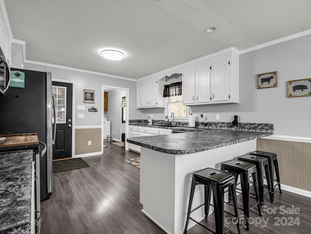 kitchen with dark wood-type flooring, kitchen peninsula, a textured ceiling, a kitchen bar, and white cabinets