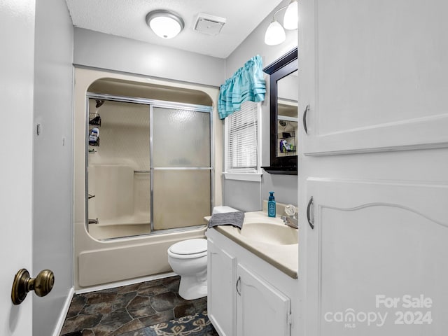 full bathroom with a textured ceiling, vanity, toilet, and bath / shower combo with glass door