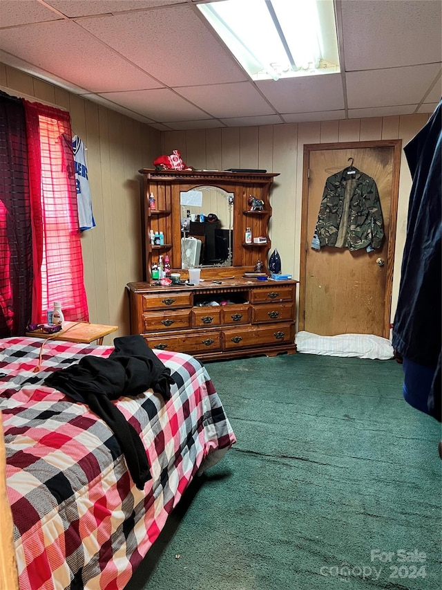 bedroom with a paneled ceiling, wooden walls, and dark carpet