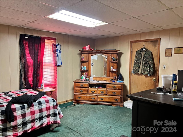 carpeted bedroom with a drop ceiling and wooden walls