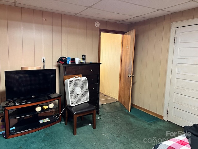 living area featuring a paneled ceiling, wooden walls, and dark colored carpet