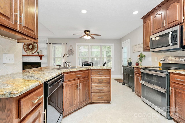 kitchen with appliances with stainless steel finishes, light stone counters, a brick fireplace, ceiling fan, and sink