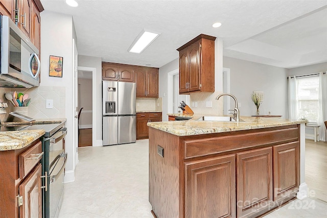 kitchen with decorative backsplash, appliances with stainless steel finishes, kitchen peninsula, light stone countertops, and sink