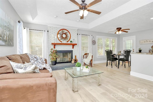 living room with a tray ceiling, ceiling fan, light hardwood / wood-style floors, and a brick fireplace