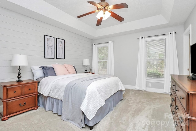 carpeted bedroom featuring a tray ceiling, ceiling fan, and wooden walls