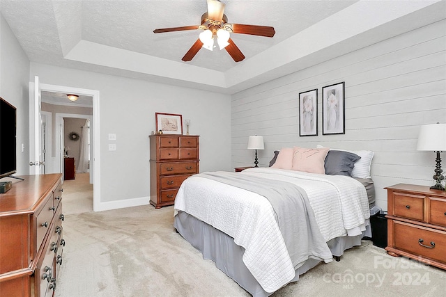 carpeted bedroom with a tray ceiling, ceiling fan, wood walls, and a textured ceiling