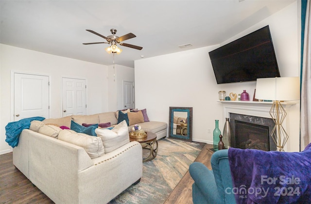 living room featuring ceiling fan, a fireplace, and dark wood-type flooring