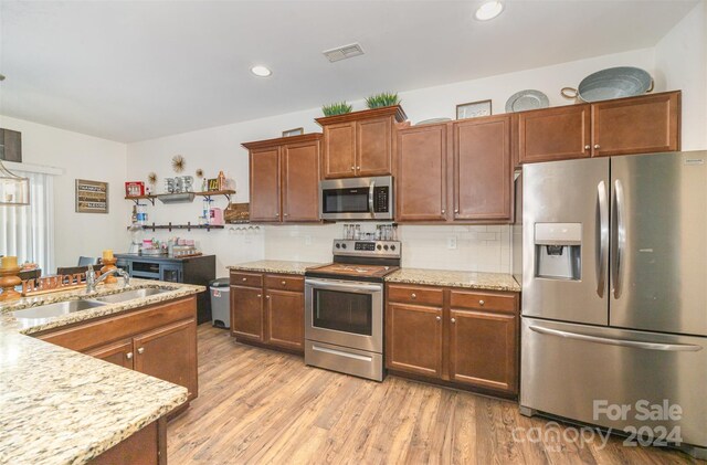 kitchen featuring sink, light hardwood / wood-style flooring, appliances with stainless steel finishes, tasteful backsplash, and light stone counters