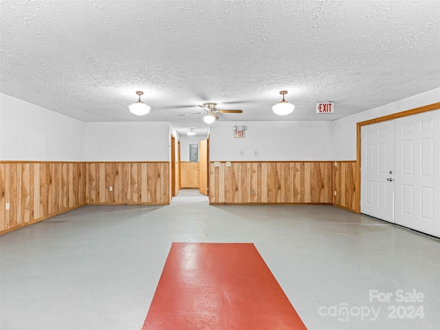 basement featuring ceiling fan, wooden walls, and a textured ceiling