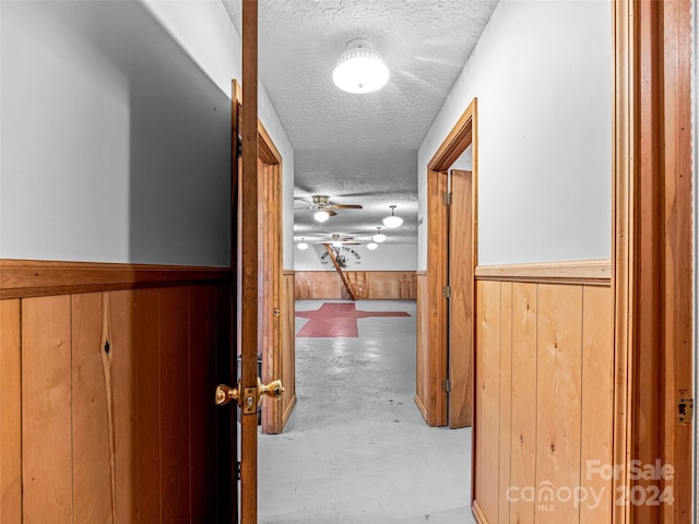 corridor with concrete flooring, a textured ceiling, and wooden walls