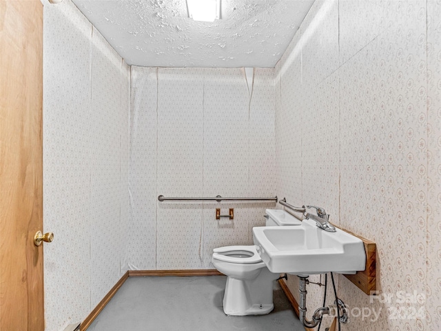 bathroom with concrete flooring, a textured ceiling, toilet, and sink