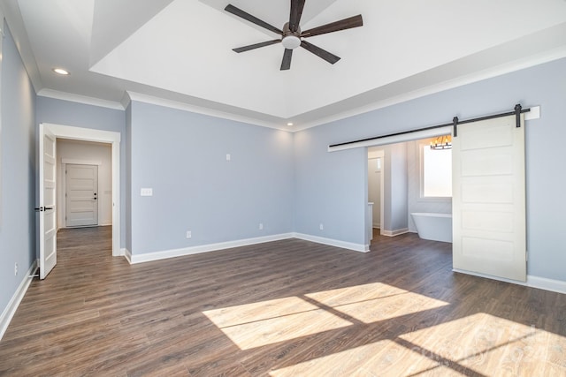 unfurnished bedroom with a barn door, dark hardwood / wood-style floors, crown molding, a tray ceiling, and ceiling fan