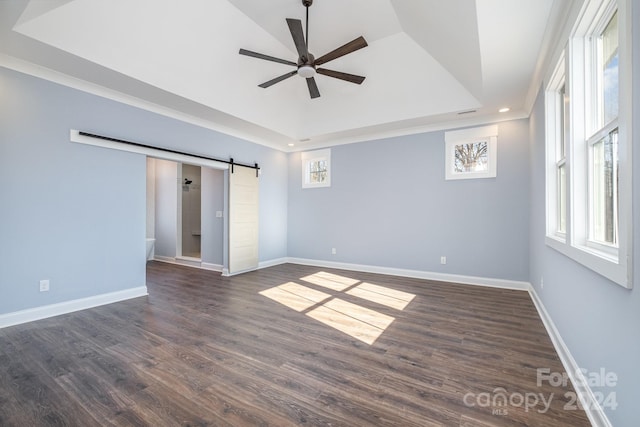 spare room with dark hardwood / wood-style flooring, a barn door, ceiling fan, and a raised ceiling