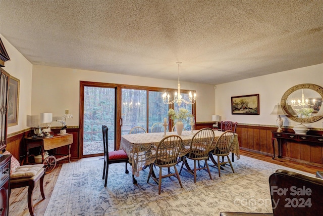 dining room featuring wood walls, a chandelier, a textured ceiling, and light hardwood / wood-style flooring