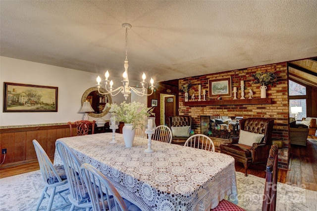 dining area featuring a textured ceiling, a notable chandelier, dark hardwood / wood-style floors, wooden walls, and a brick fireplace