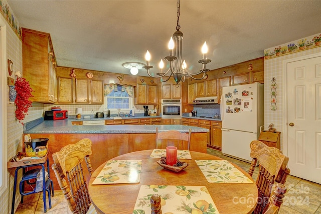 kitchen with white refrigerator, an inviting chandelier, kitchen peninsula, oven, and ventilation hood